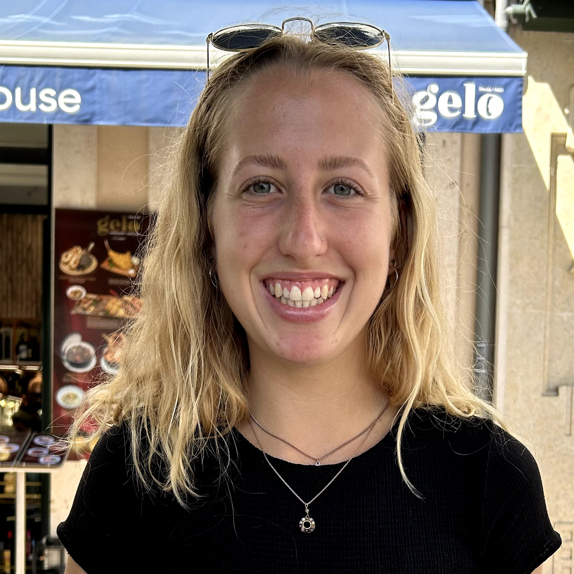 Picture of a smiling person with long strawberry blonde straight hair, fair skin, a black shirt and blue jeans against a pink background.