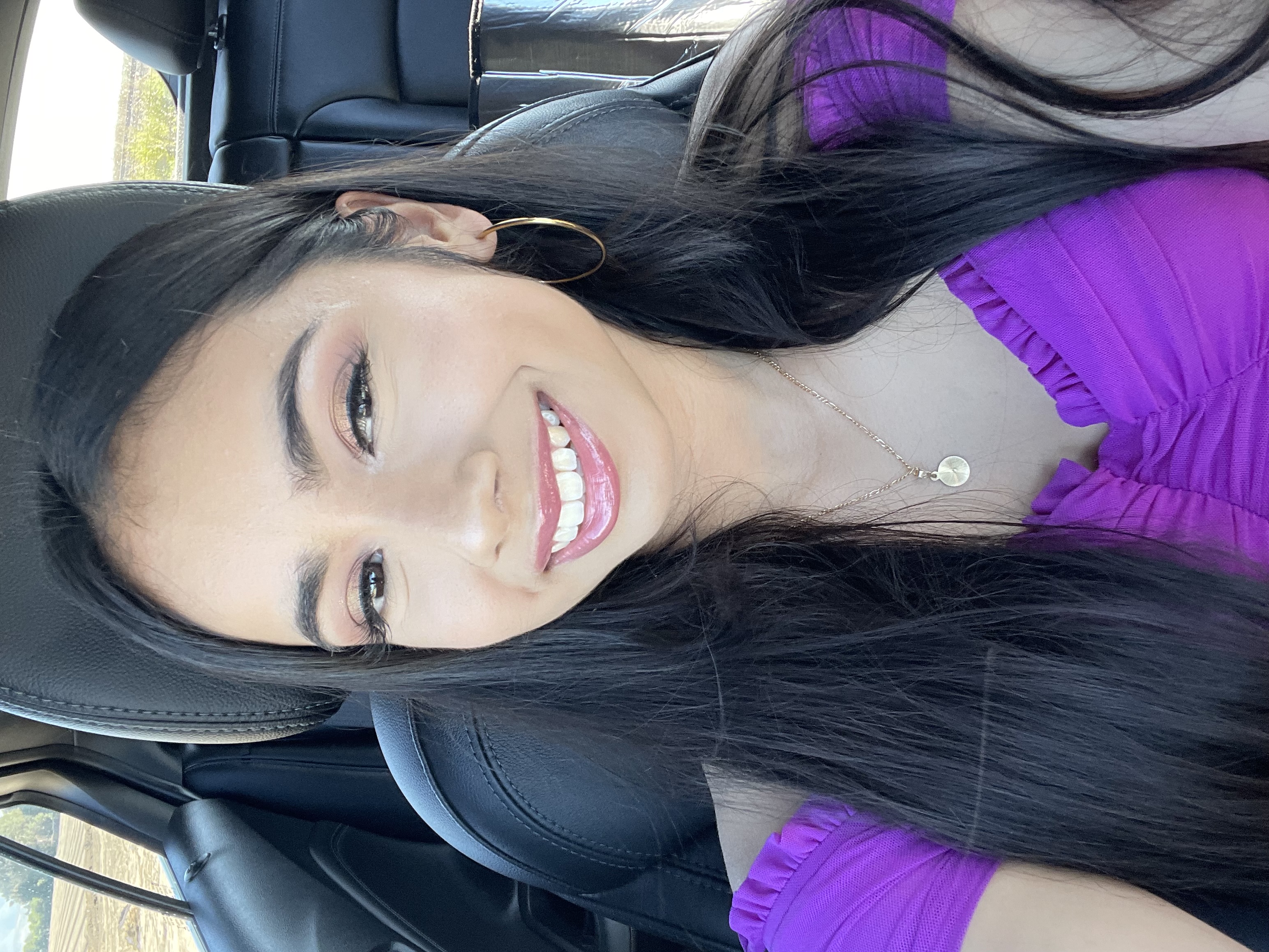 Picture of a smiling person with dark long hair in a car.