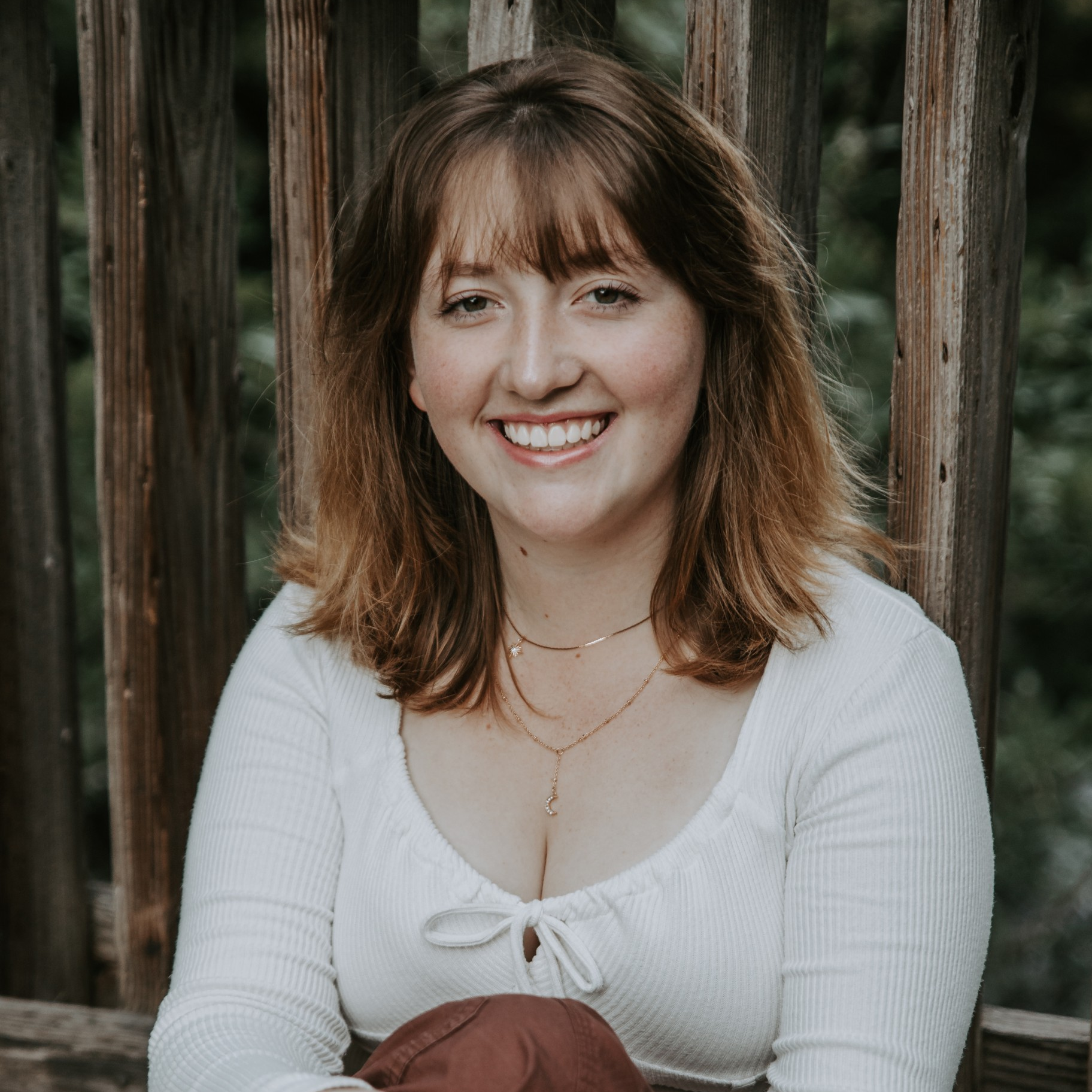 Picture of a smiling person with long dark hair, fair skin, a black shirt and blue jeans against a pink background.