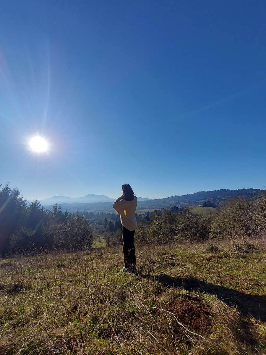 A person facing the horizon wearing a beige sweater and a clear, sunny sky above.